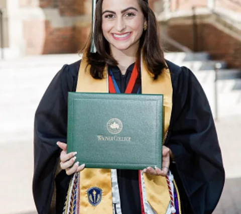 Holding her diploma in graduation regalia with an Honor Society stole