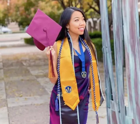 In graduation regalia with an Honor Society stole, medallion and cords